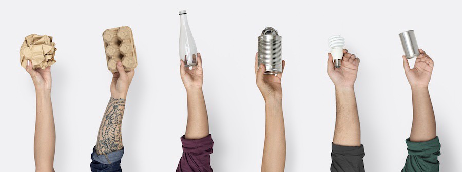 hands holding up paper, bottle, cans and light bulb to show many items can be recycled at home